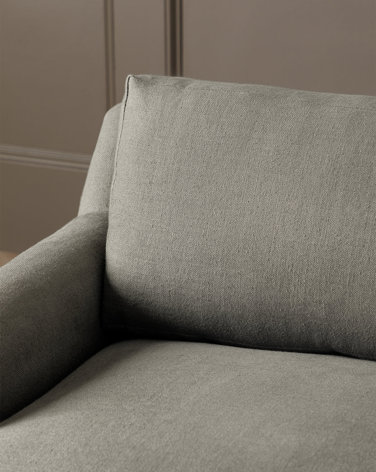 Close-up of the Lucille English Roll Arm Chair and a Half, featuring gray upholstery, a cushioned down-wrapped seat, soft backrest and armrests, set against a plain beige paneled wall, by McGee & Co.
