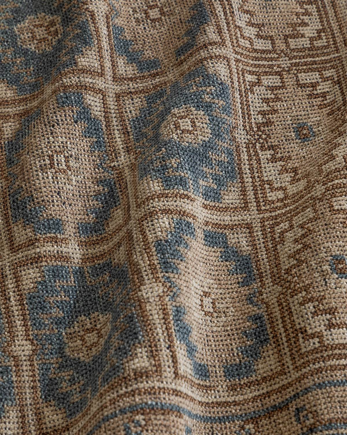 A close-up of the Nunez Hand-Knotted Wool Rug, showing its geometric pattern in muted blue and beige tones, woven texture, and subtle fabric folds, by McGee & Co.