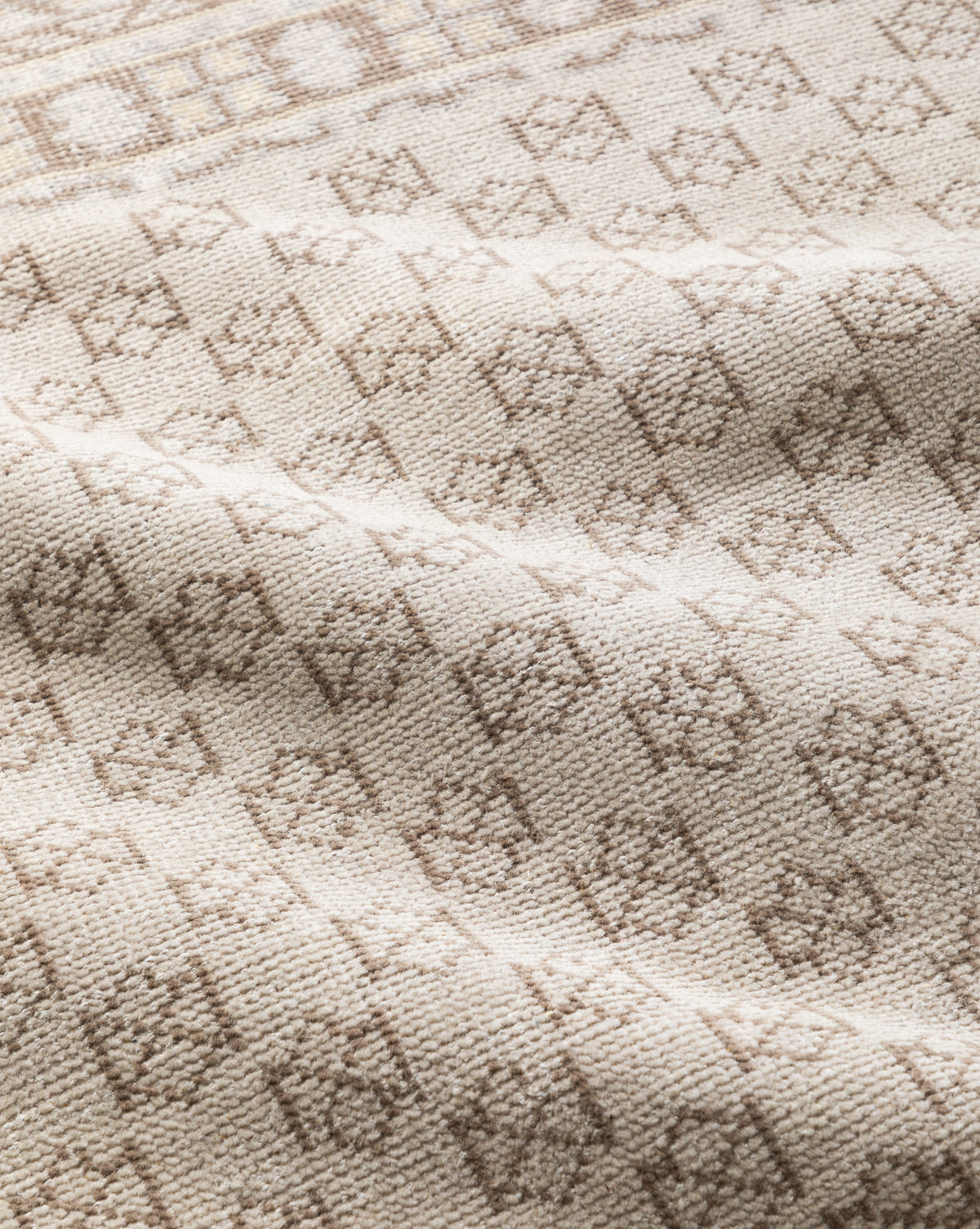 A close-up of the Anya Neutral Hand-Knotted Wool Rug displays beige woven wool with a subtle light brown diamond pattern, gentle folds, and a soft texture, by McGee & Co.