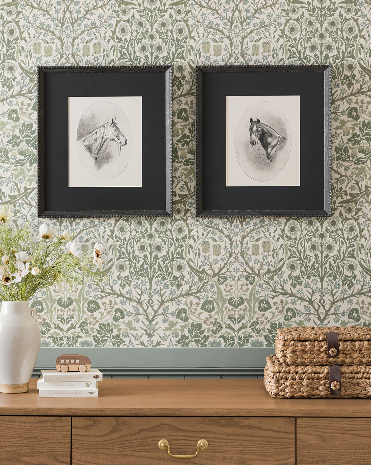 The Winnie framed horse portraits in black frames hang on a green floral wallpapered wall above a wooden dresser. A vase with flowers and stacked woven baskets sit atop, complementing the elegant Winnie wall art display by McGee & Co.