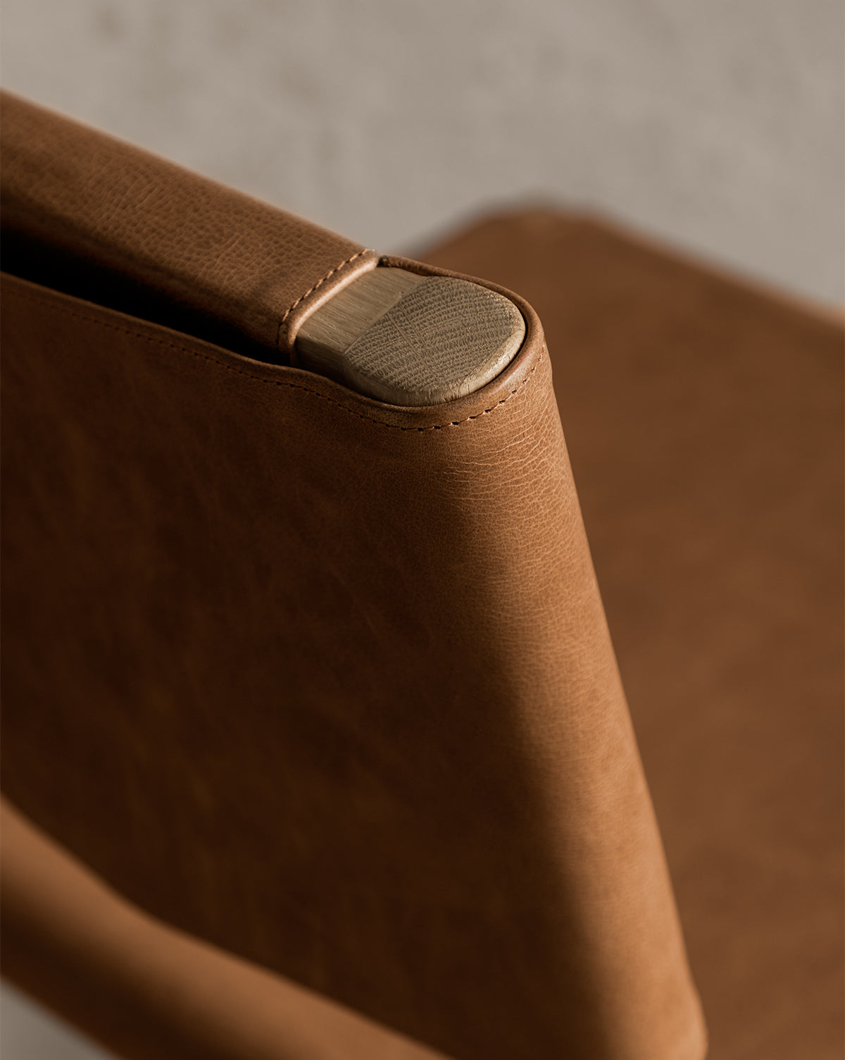 A close-up of the Danson Counter Stool highlights its brown leather seat backrest with visible stitching, elegantly wrapped around a wooden frame, set against a neutral background to showcase its minimalist design by McGee & Co.