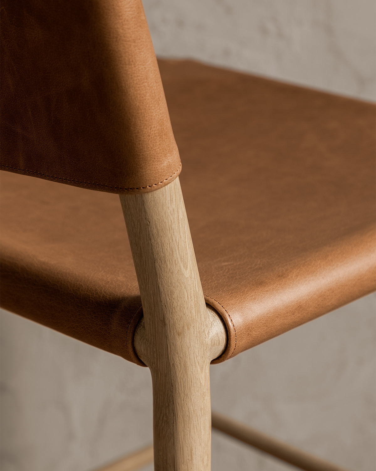 Close-up of the Danson Counter Stool, showcasing its minimalist design with light wood legs and a smooth brown leather seat and backrest, emphasizing quality craftsmanship and rich textures, by McGee & Co.