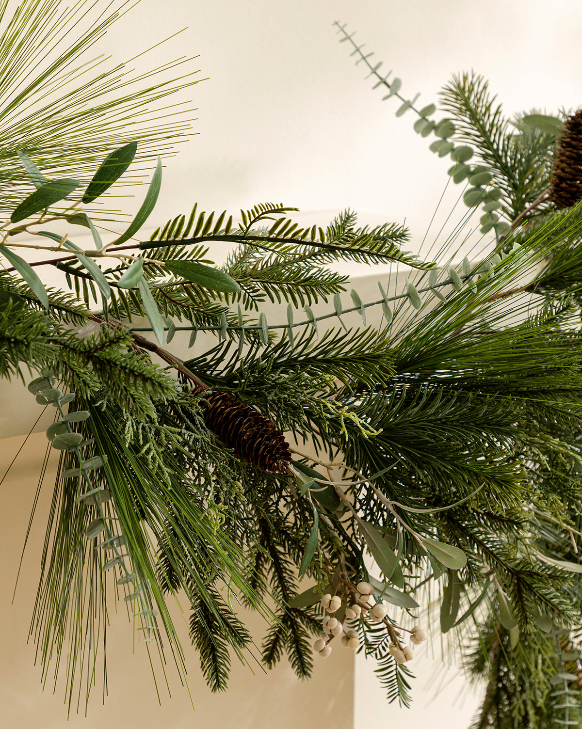 The 6' Pinecone & Berries Faux Garland features festive pine branches and red berries, ideal for bringing holiday charm to your space when draped along a light-colored wall, by McGee & Co.