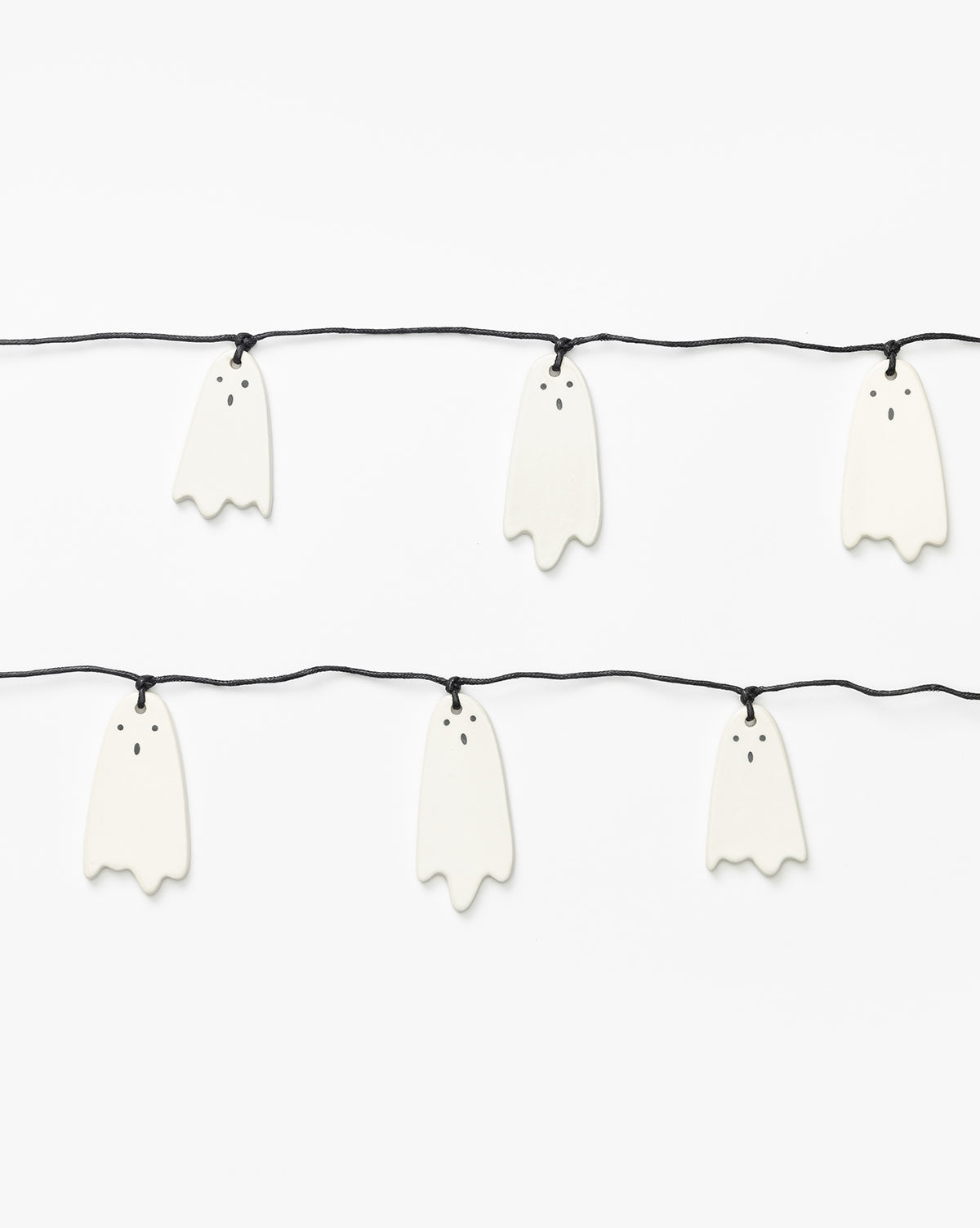 The 3 Ceramic Ghost Garland features cute white ghosts with hand-detailed faces—two black eyes and a round mouth—strung on two black cords against a plain background, making it perfect for charming Halloween decor, by McGee & Co.