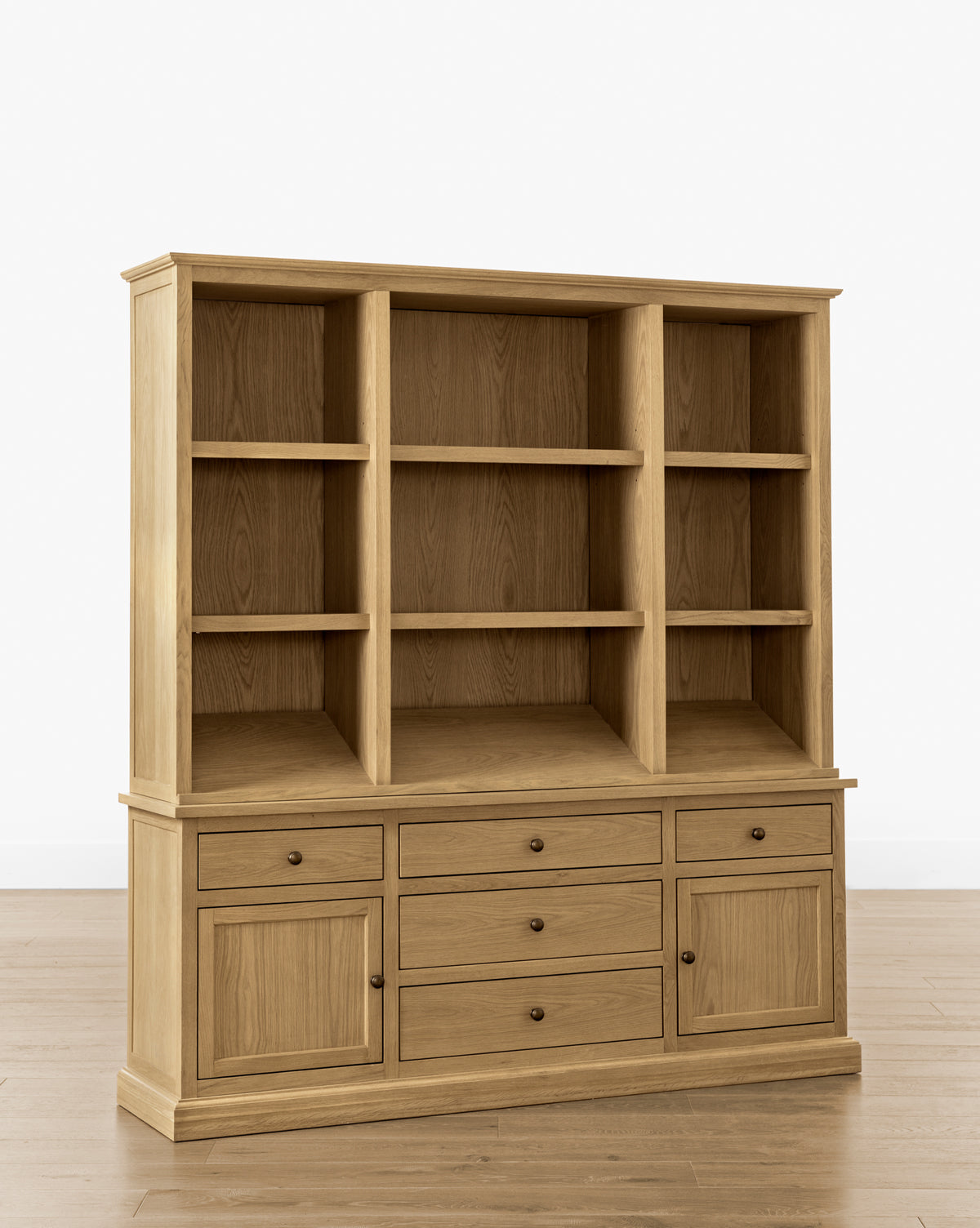 The Adler Oak Cabinet stands on a wooden floor against a plain white background, featuring three open shelves above and a lower section with six drawers and three cabinet doors for ample storage space, by McGee & Co.