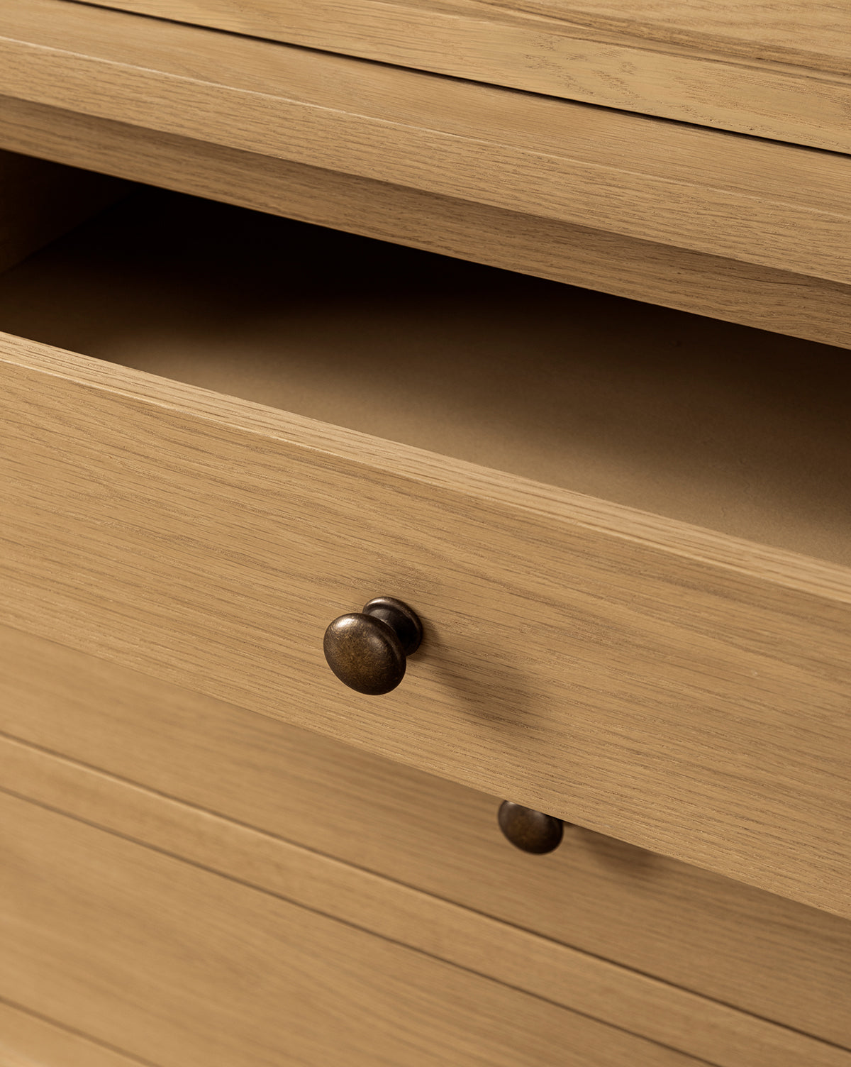 A close-up of the Adler Oak Cabinet shows a partially open drawer with empty storage space inside. The drawer has a round, dark knob handle, and the cabinet features a light, natural oak finish by McGee & Co.