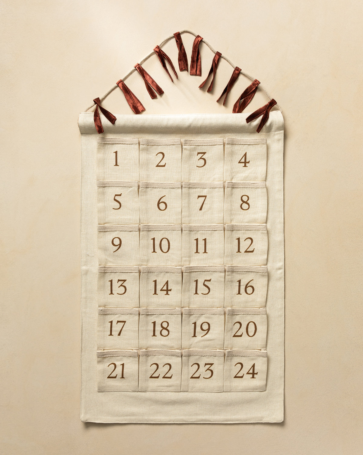 The Advent Calendar is a cream-colored cotton linen piece with 24 numbered pockets in a grid, hanging from a rod with brown ribbons—a charming way to count down to Christmas, by McGee & Co.