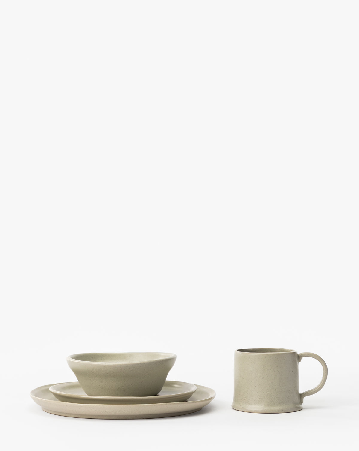 The Aiden Soft Gray Side Plate, in a minimalist design, is showcased with a classic round plate, mug, bowl, and stacked plates, all arranged neatly against a plain white background in soft gray tones, by McGee & Co.