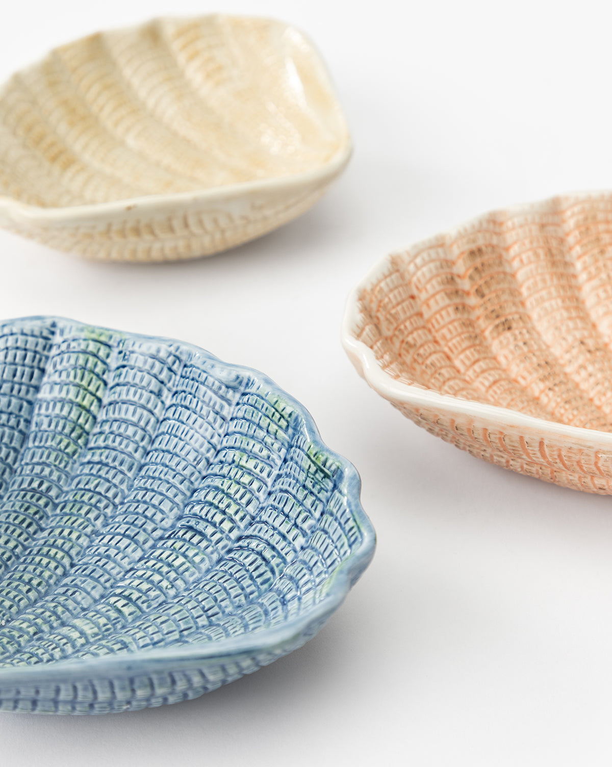 The Aurelie Shell Shaped Bowls (Set of 4) feature coastal-inspired stoneware with a ridged, woven texture. The set includes blue, light yellow, and peach bowls, adding seaside charm to your table by McGee & Co.