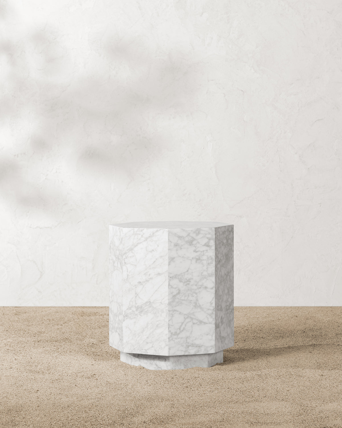 The Barcelo Outdoor Side Table, crafted from white marble with subtle grey veining, features a geometric design and stands on a sandy surface against a textured off-white wall, by McGee & Co.