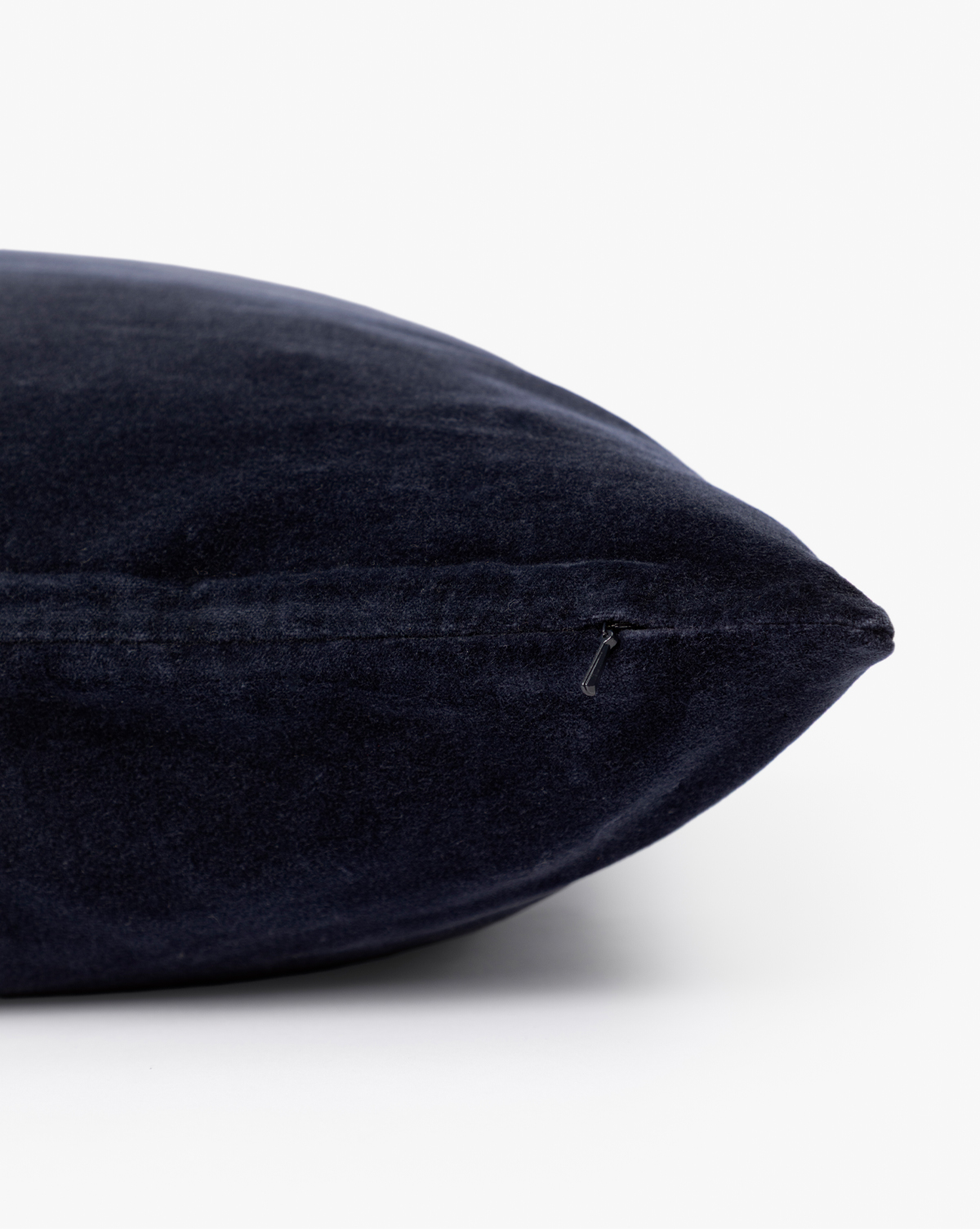 A close-up of the Bellevue Velvet Pillow Cover in dark navy blue shows its side zipper, set against a plain white background—ideal as a stylish decorative accent for your sofa, by McGee & Co.