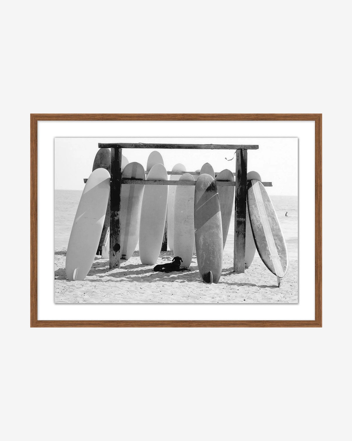 Boards at the Ready—a black and white photo of surfboards upright in a beachside wooden rack, the ocean in view, framed in a brown wooden frame—captures iconic surf culture, by McGee & Co.