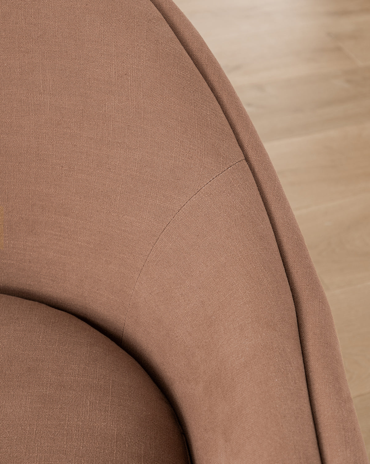 Close-up of the curved armrest and backrest of the Bunnell Lounge Chair (Ready to Ship), a modern-traditional chair in brown fabric upholstery, with wooden flooring visible in the background by McGee & Co.