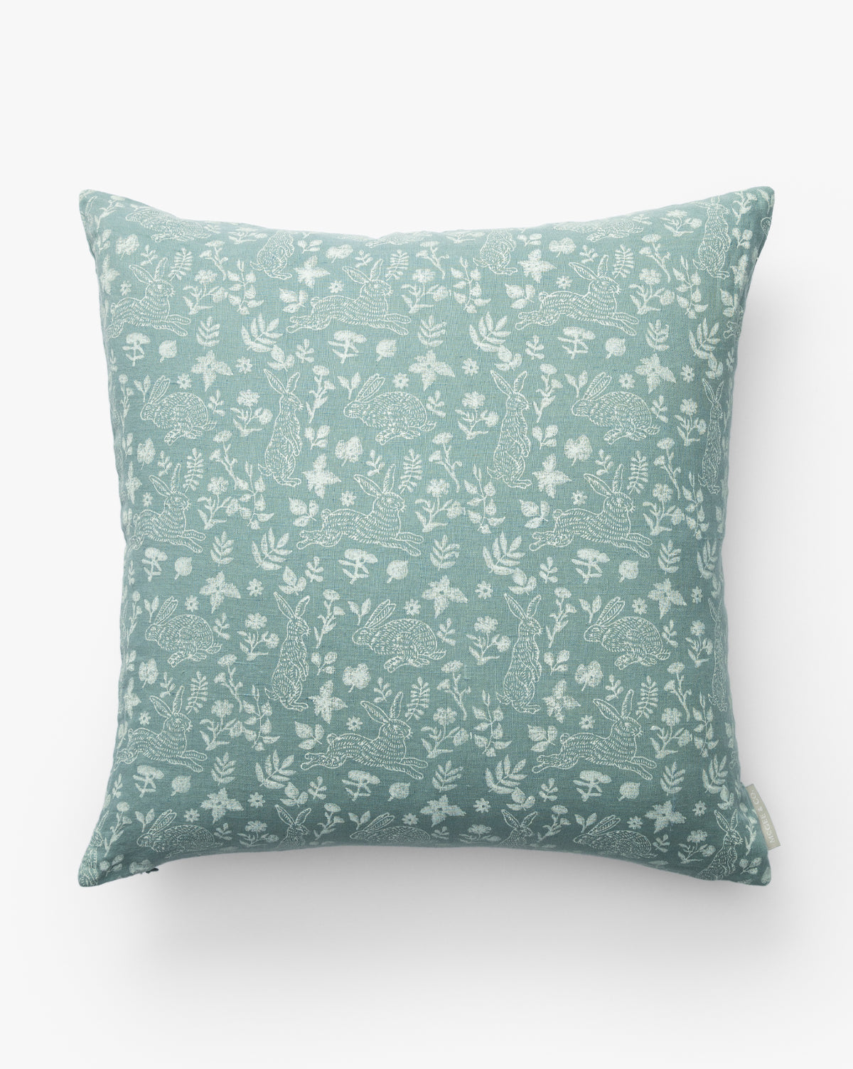 The Bunny Blockprint Pillow Cover features a square, light blue-green design with white rabbits, hedgehogs, mushrooms, and plants in a nature-inspired block print on white linen, by McGee & Co.
