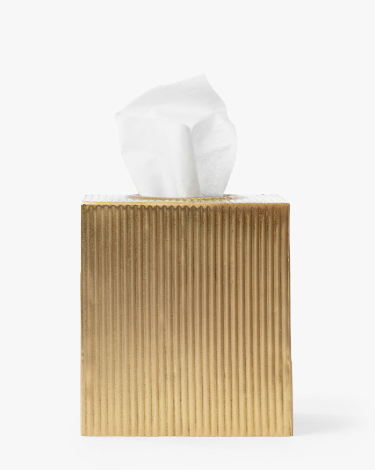 The Calvert Brass Tissue Box Cover, featuring a gold fluted design and white tissue emerging from the top, creates an elegant accent against a plain white background, by McGee & Co.