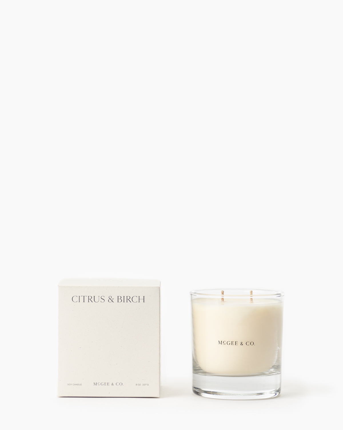 A white box labeled Citrus & Birch Candle sits beside a McGee & Co. luxury glass jar candle made from soy wax with two wicks, both displayed against a plain white background by McGee & Co.