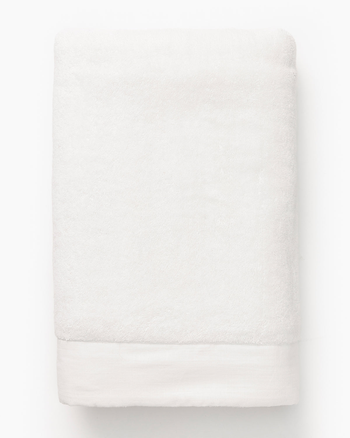 A folded white cotton towel from the Dedra Bath Collection with a smooth, plain surface and a wide flat border at one end rests on a white background.