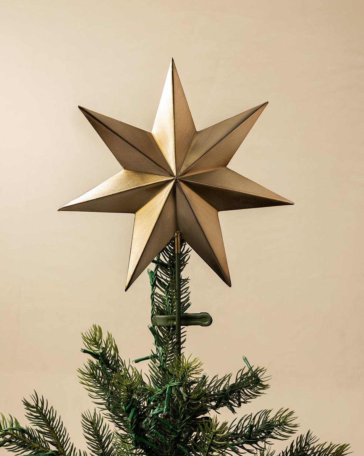 An Etoile Tree Topper with an aged brass finish crowns a green holiday tree, against a plain beige background, by McGee & Co.