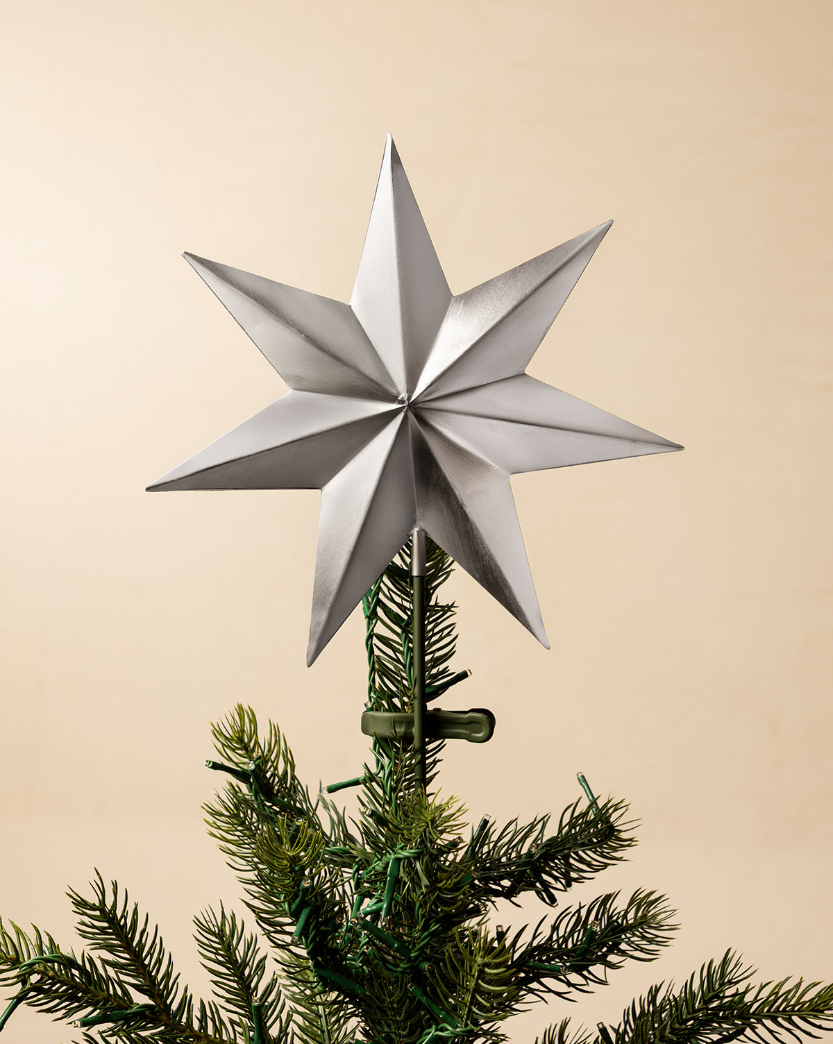 The Etoile Tree Topper in aged brass crowns a green artificial holiday tree branch, displayed against a plain beige background, by McGee & Co.