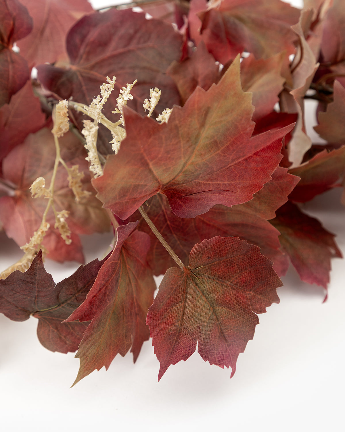 The Faux Autumn Grapevine Stem features rust-hued red and brown leaves with cream-colored flowers, elegantly arranged on a white background—perfect for stylish fall decor, by McGee & Co.