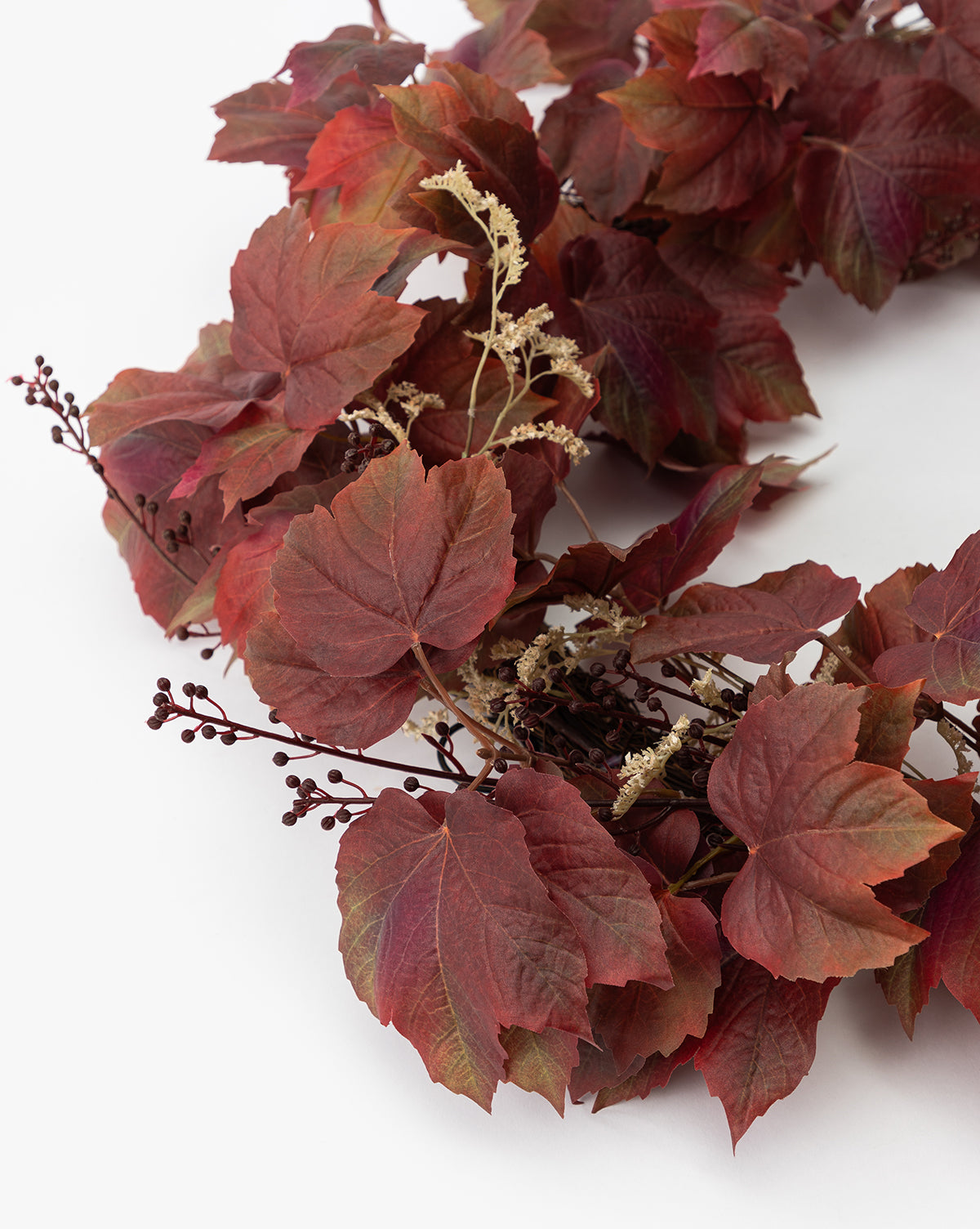 A close-up of the Faux Autumn Grapevine Wreath, adorned with deep red and burgundy leaves, brown berries, cream dried flowers, and faux greenery—ideal for seasonal decor against a white background.