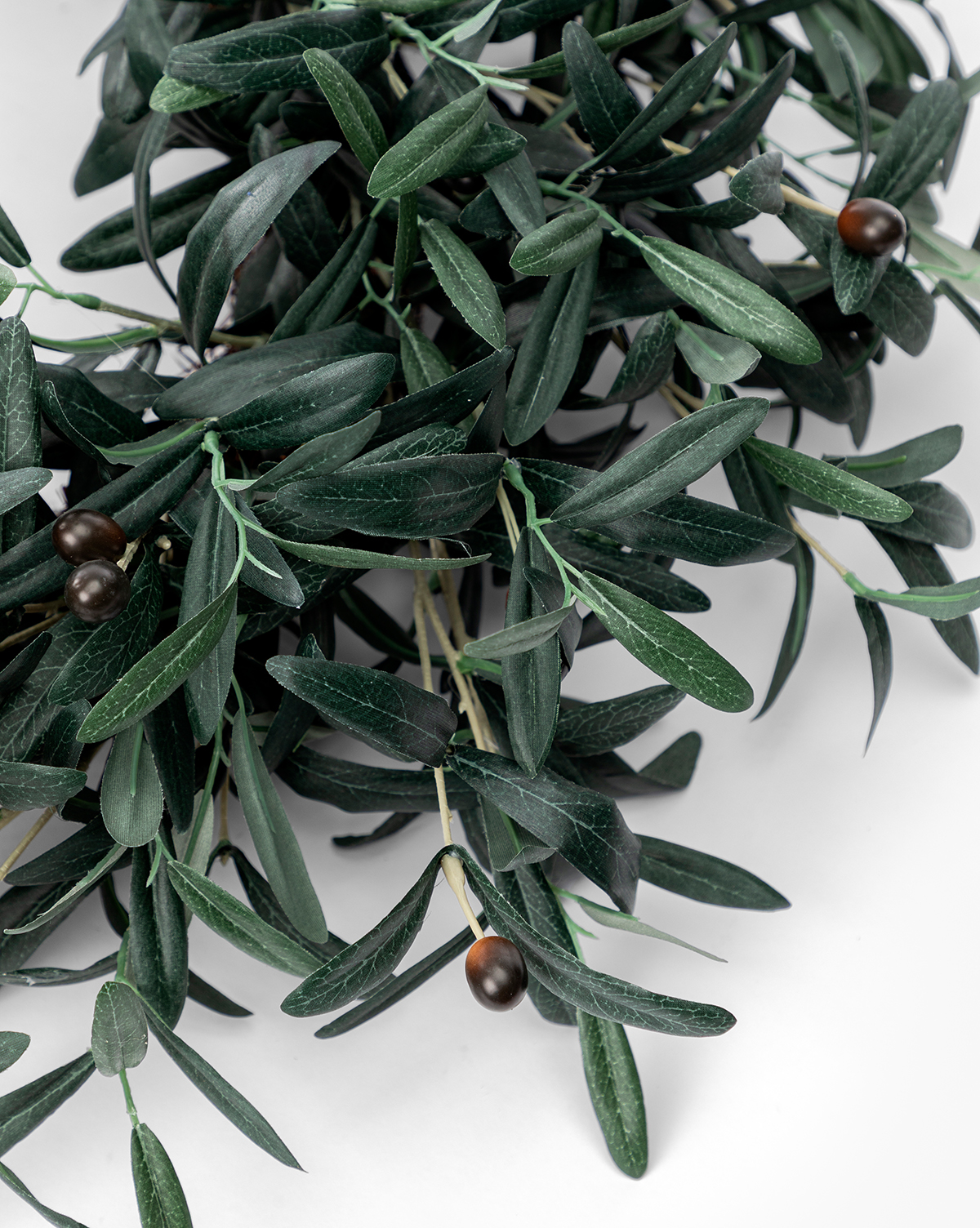 A close-up of the Faux Olive Berry Wreath, displaying lifelike green olive branches and dark olives on a white background. The long, narrow leaves and realistic berries range in color from dark brown to black, by McGee & Co.