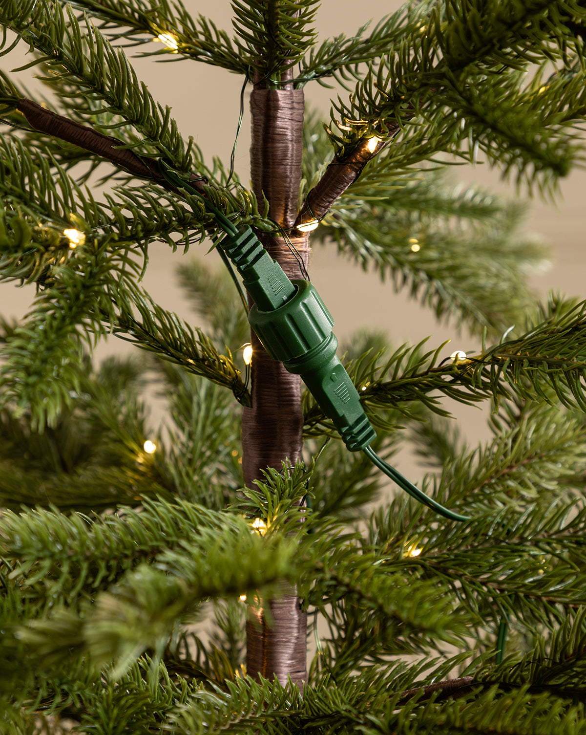 Close-up of a green electrical plug connected to a matching socket on the trunk of the Faux Spruce Pre-Lit Potted Tree, with small string lights woven among its lush branches, by McGee & Co.