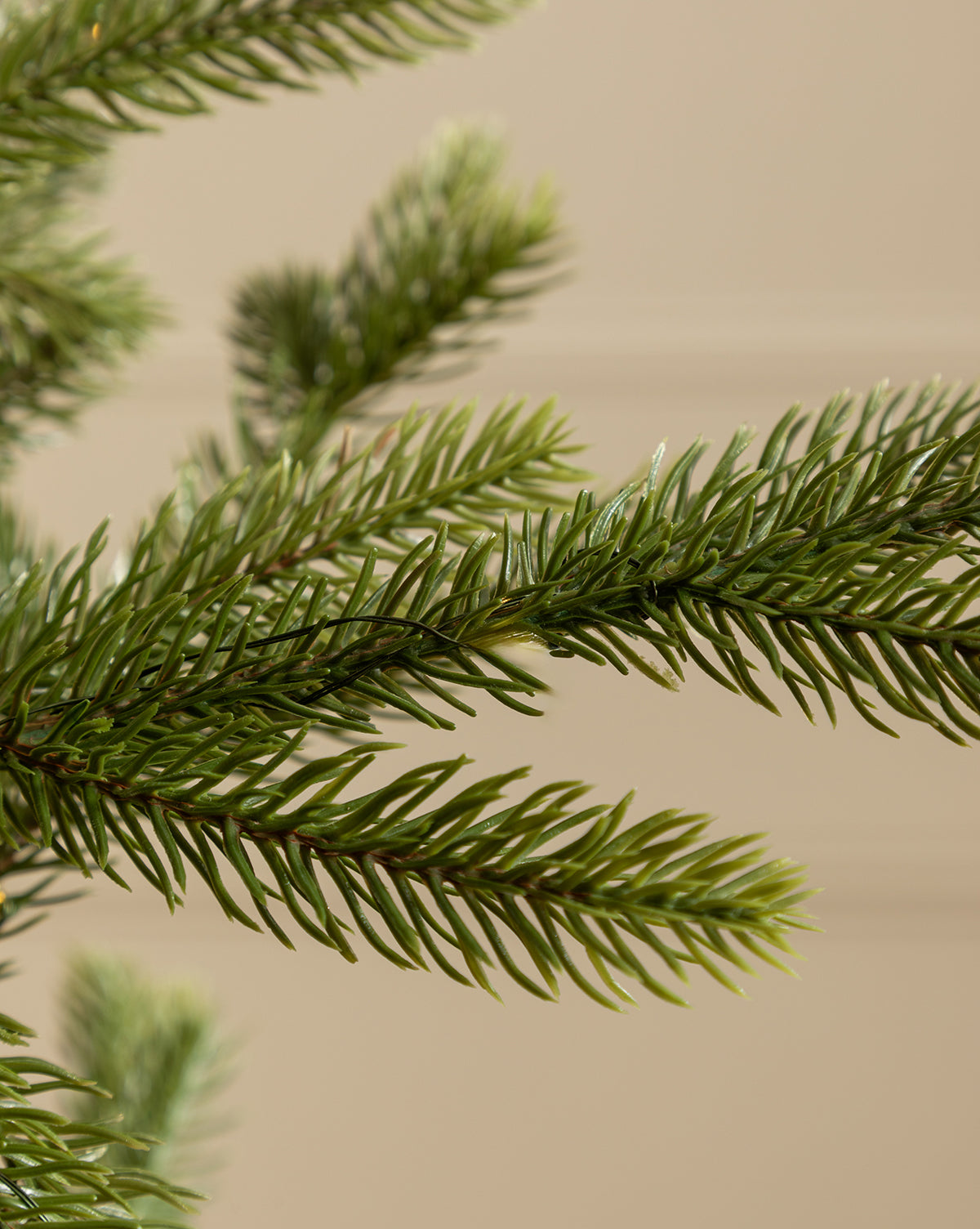 Close-up of dense green needles on the Faux Spruce Pre-Lit Potted Tree, with realistic artificial evergreen branches set against a neutral beige background, by McGee & Co.