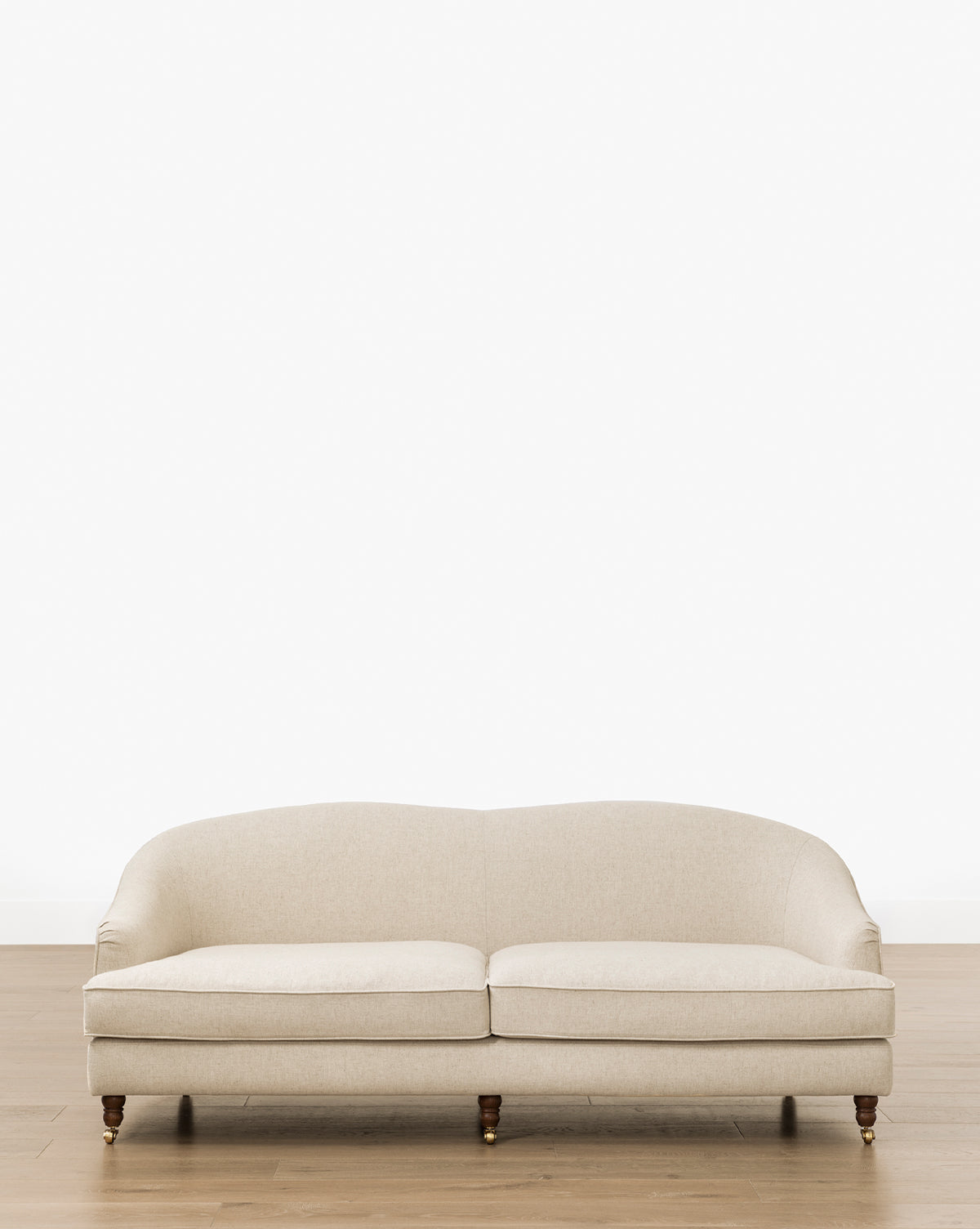 The Makerspalm Fletcher Sofa 76 (Ready to Ship) features a beige upholstered finish, curved backrest, and wooden legs. It sits on a light wood floor against a plain white wall, adding handcrafted, customizable style to any space by McGee & Co.