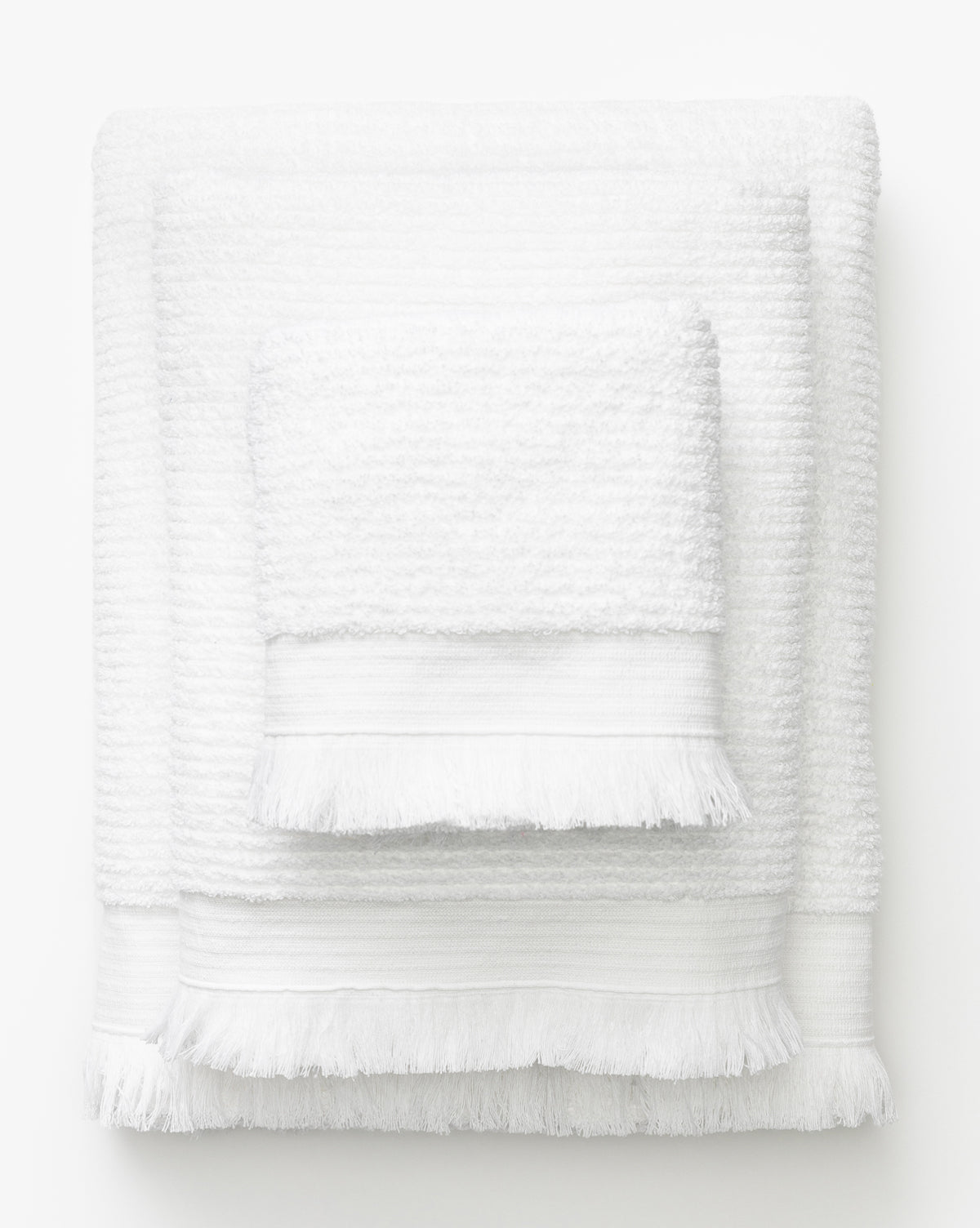 Three white towels of varying sizes from the Frayser White Bath Collection, each featuring fringed edges, are stacked together against a plain white background—an elegant addition to your bath essentials, by McGee & Co.