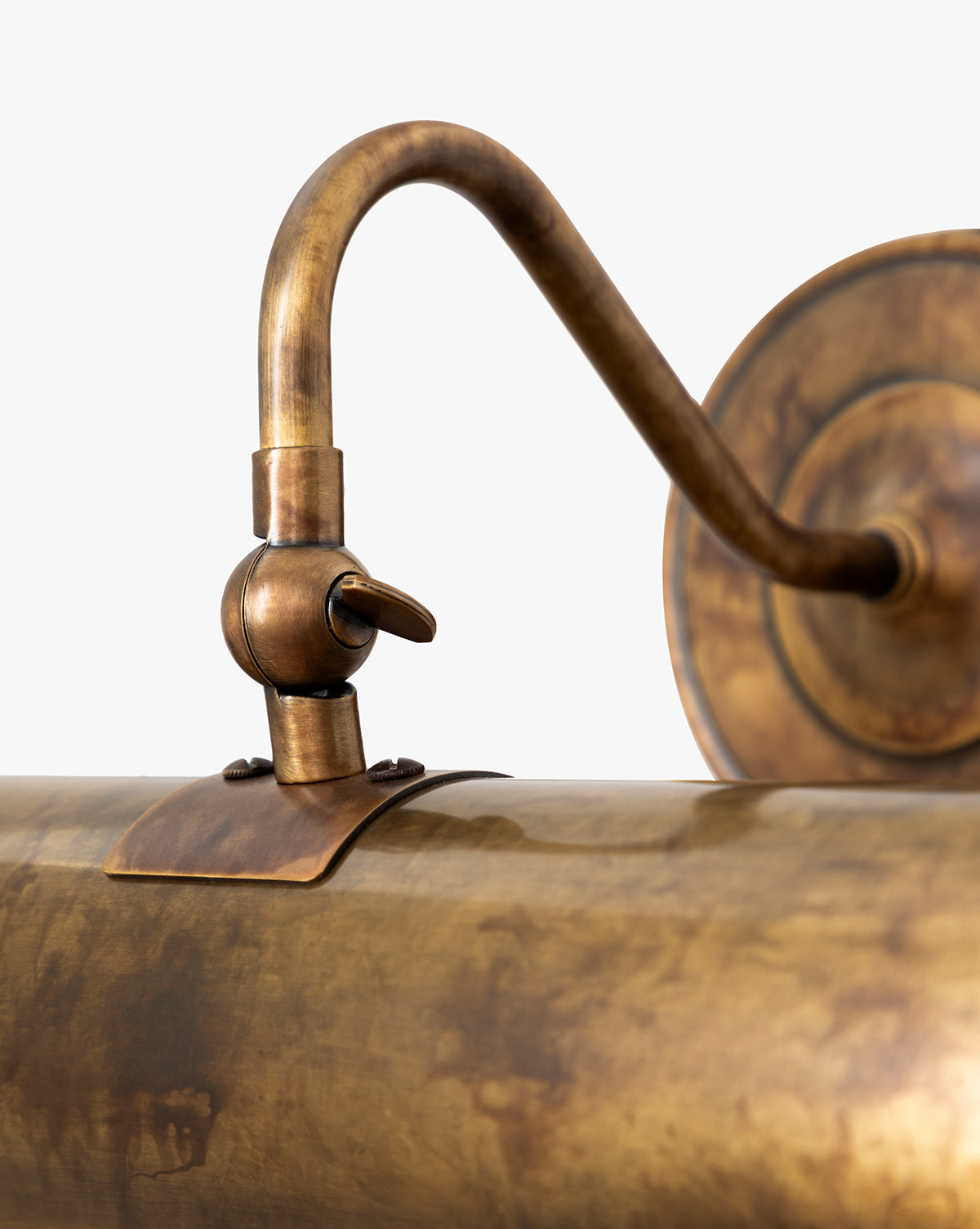 Close-up of the Gallery Picture Sconce in burnished bronze, featuring a curved arm, cylindrical shade, weathered patina finish, and detailed metalwork set against a plain background, by McGee & Co.