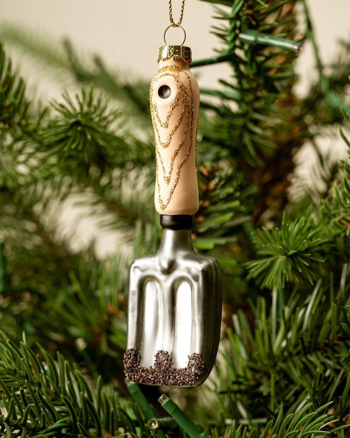 The Gardeners Ornament is a Christmas tree ornament shaped like a garden trowel with a glittery handle, perfect for hanging on your tree—a charming holiday gift for any gardener, by McGee & Co.