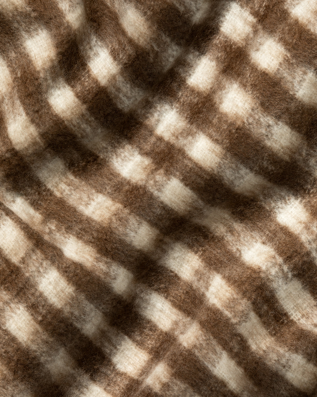 A close-up of the Indaba Gingham Wool Blend Throw, showcasing its soft, fuzzy texture and brown and cream checkered pattern with gentle folds for a cozy feel. McGee & Co.