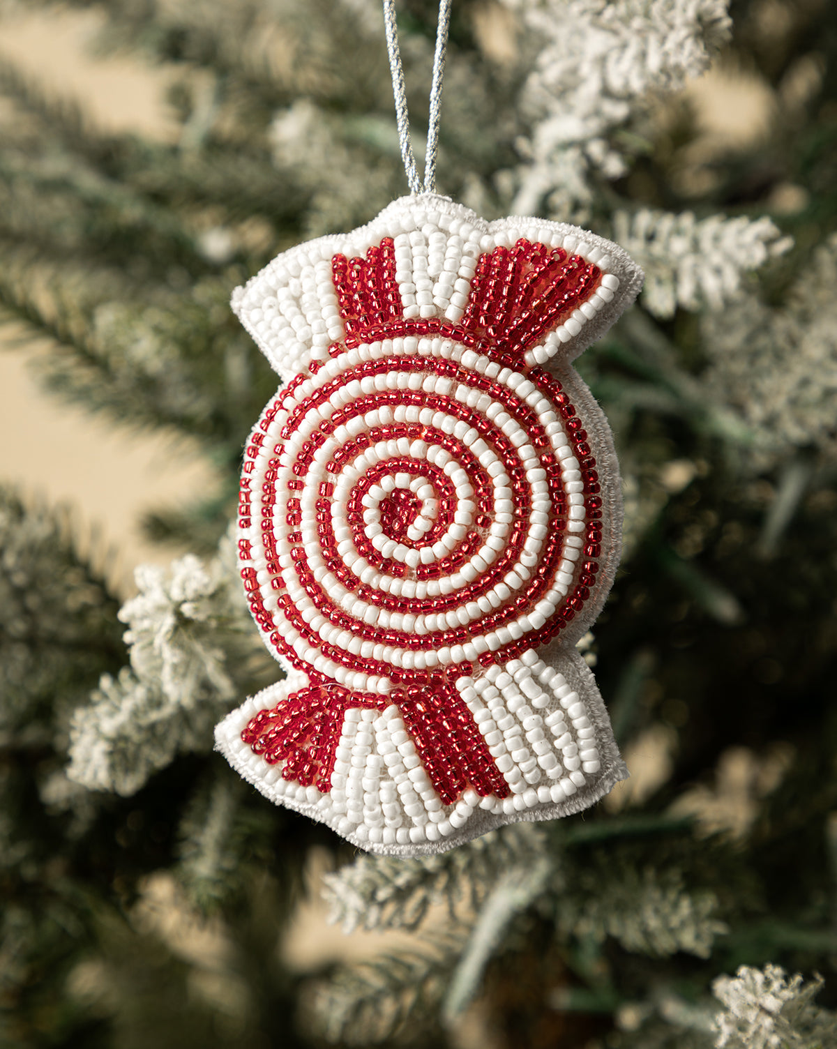 The Handmade Beaded Candy Fabric Ornaments (Set of 3) feature red and white spiral designs, adding festive charm to your holiday décor when hung on a snow-frosted Christmas tree branch, by McGee & Co.