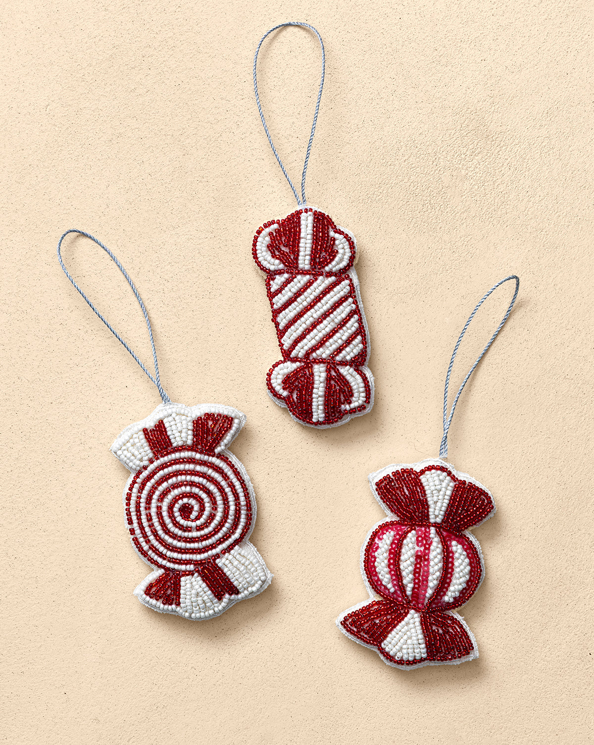 The Handmade Beaded Candy Fabric Ornaments (Set of 3) feature red and white candy shapes with silver hanging loops, displayed on a light beige background—unique holiday tree decorations, by McGee & Co.