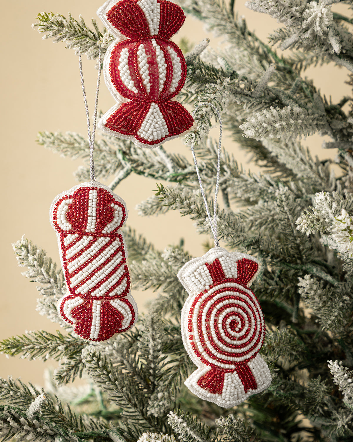Add a festive touch to your tree with the Handmade Beaded Candy Fabric Ornaments (Set of 3)—red and white, candy-shaped decorations featuring spiral and striped patterns that look charming on snowy branches, by McGee & Co.