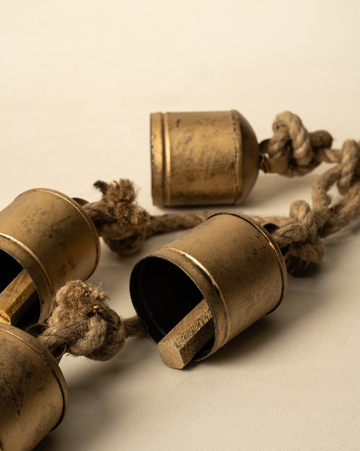 A close-up of three Hanging Iron Bells, featuring a weathered gold finish and wooden clappers, each strung on a thick coarse rope. Perfect for adding antique charm to your holiday décor, by McGee & Co.