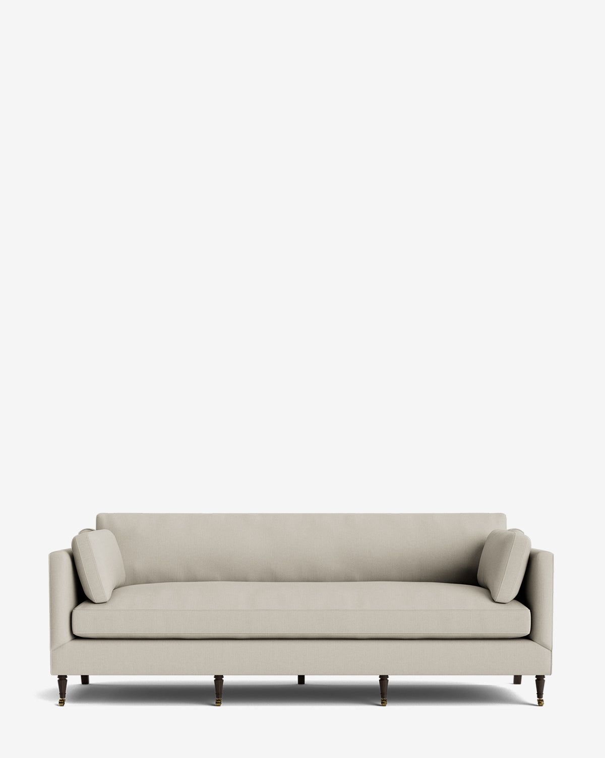 The Haverford Upholstered Sofa 90 is a modern beige handcrafted sofa featuring slim arms, two matching bolster pillows, and wooden legs with brass castors, shown against a plain white background by McGee & Co.