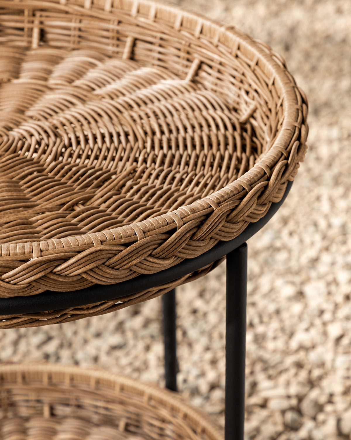 Close-up of the Haviland Bar Cart featuring weather-resistant round wicker with a braided edge, black metal legs, and a tightly woven surface—ideal for outdoor entertaining against a blurred gravel or pebble ground, by McGee & Co.