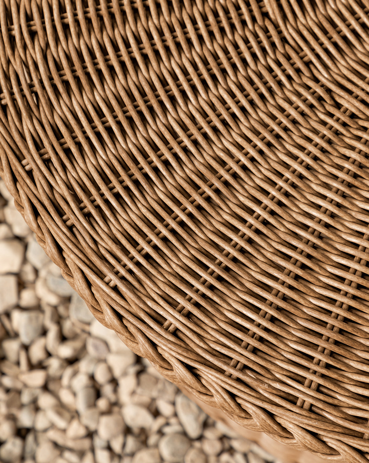 Close-up of the Haviland Coffee Table, featuring weather-resistant, tightly woven light brown wicker, set against a backdrop of small, light-colored pebbles, by McGee & Co.