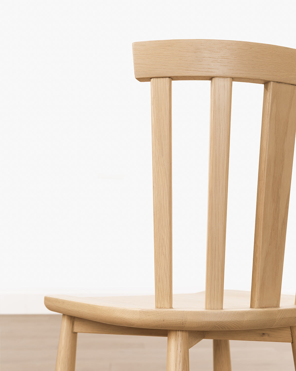 A close-up of the Hemingway Stool, crafted from solid wood with vertical back slats, stands against a plain light wall and wooden floor; only part of the stool is visible, hinting at its placement near kitchen counters, by McGee & Co.