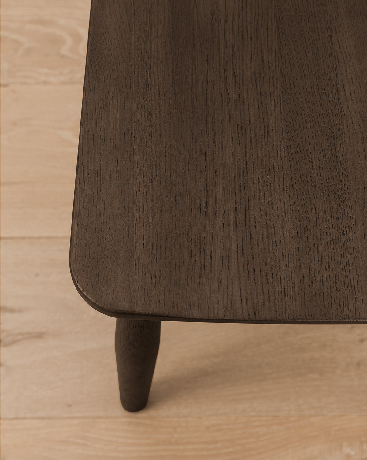 A close-up of the corner of a solid wood table with rounded edges and a visible leg on a light wood floor—an elegant accent beside kitchen counters or perfectly paired with the Hemingway Stool, by McGee & Co.