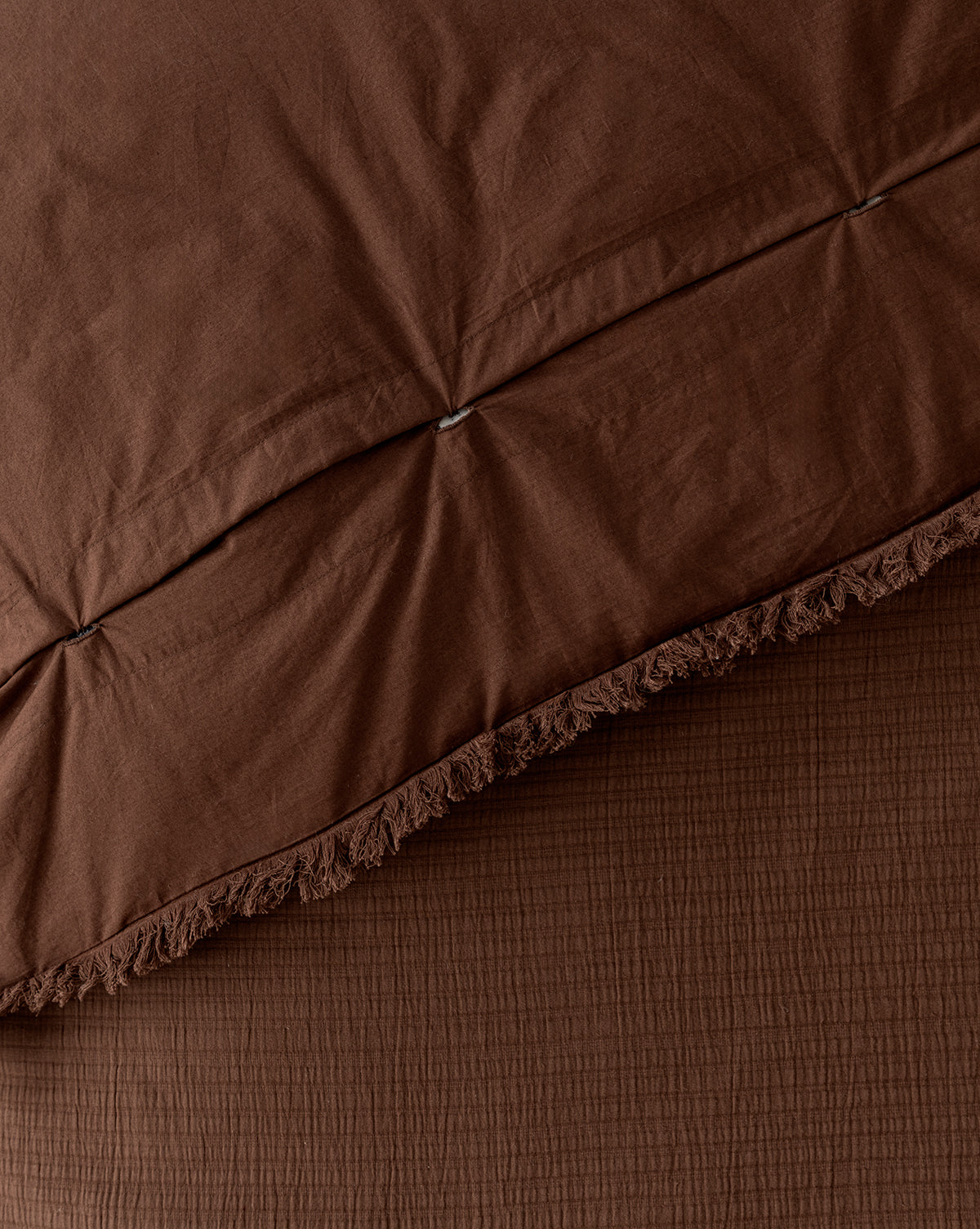 Close-up of the Hendricks Chocolate Cotton Duvet Cover, featuring a textured finish with decorative fringe along the edge, layered over a matching brown sheet for a cozy, coordinated look.