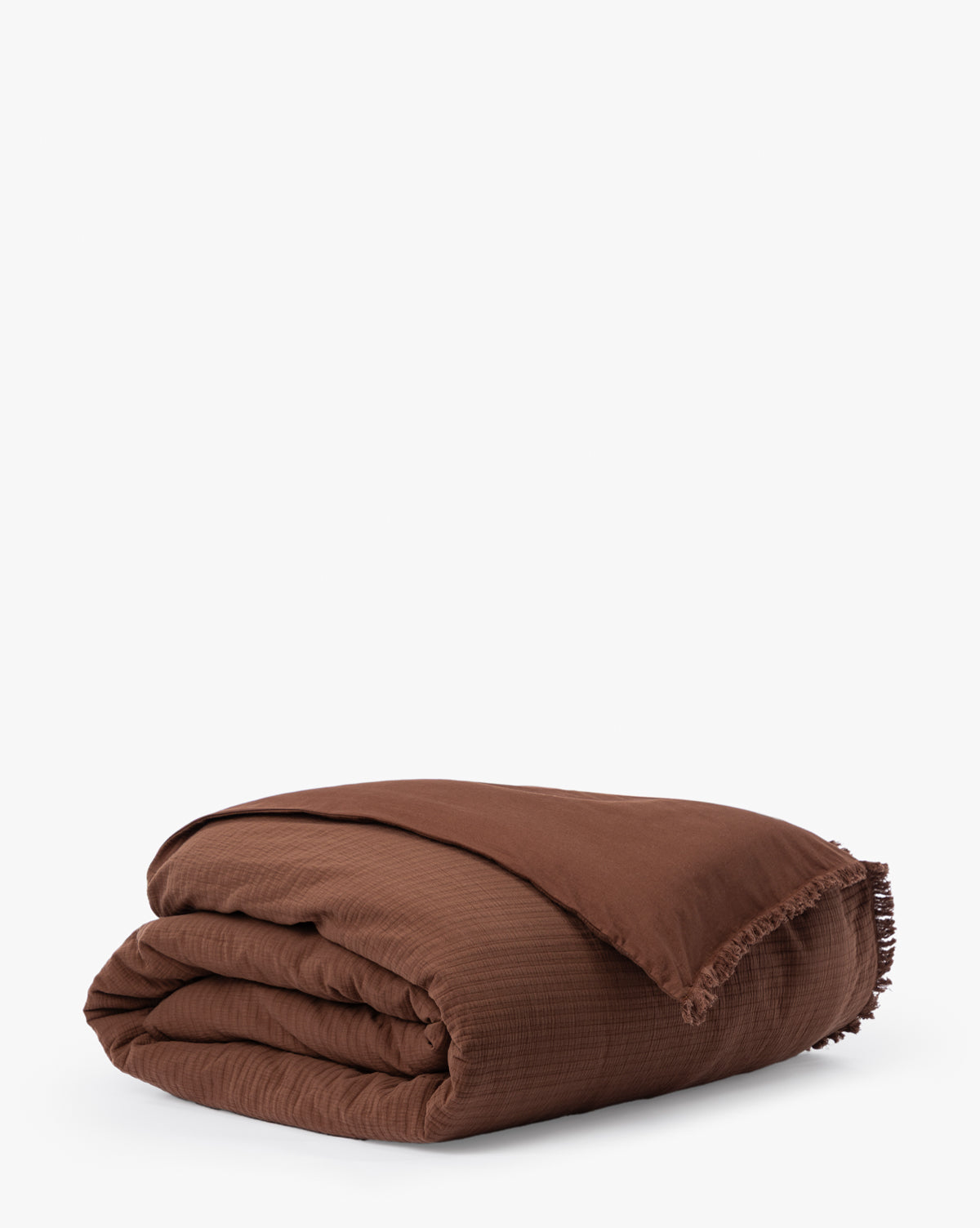 The Hendricks Chocolate Cotton Duvet Cover, featuring a slightly textured brown fabric and fringe along the edge, is folded neatly against a plain white background.