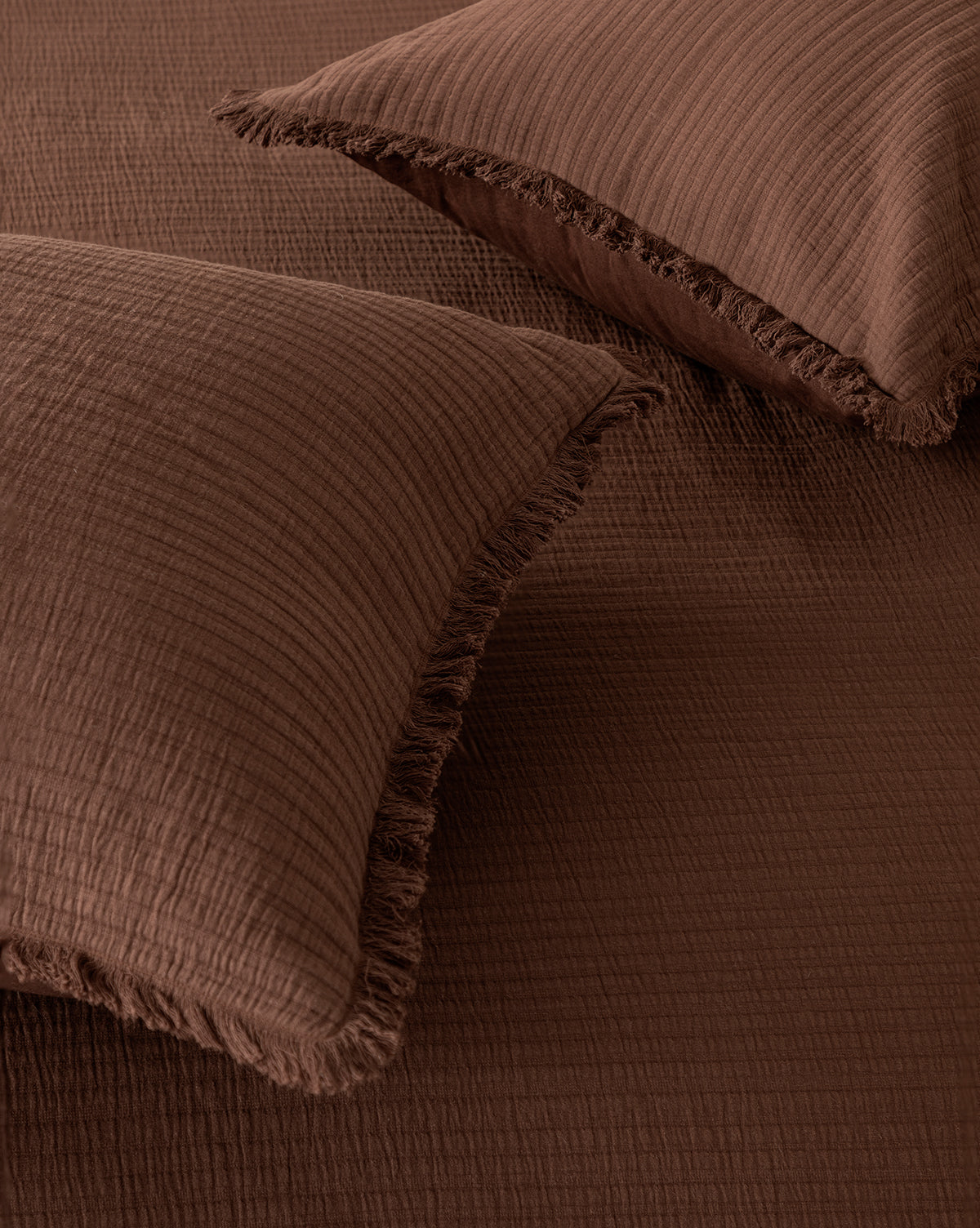 Two Hendricks Chocolate Cotton Shams (Set of 2) rest on matching cotton bedding. Made of 100% cotton with a crinkled, grid-like pattern and fringed edges, they create a cozy and inviting look.