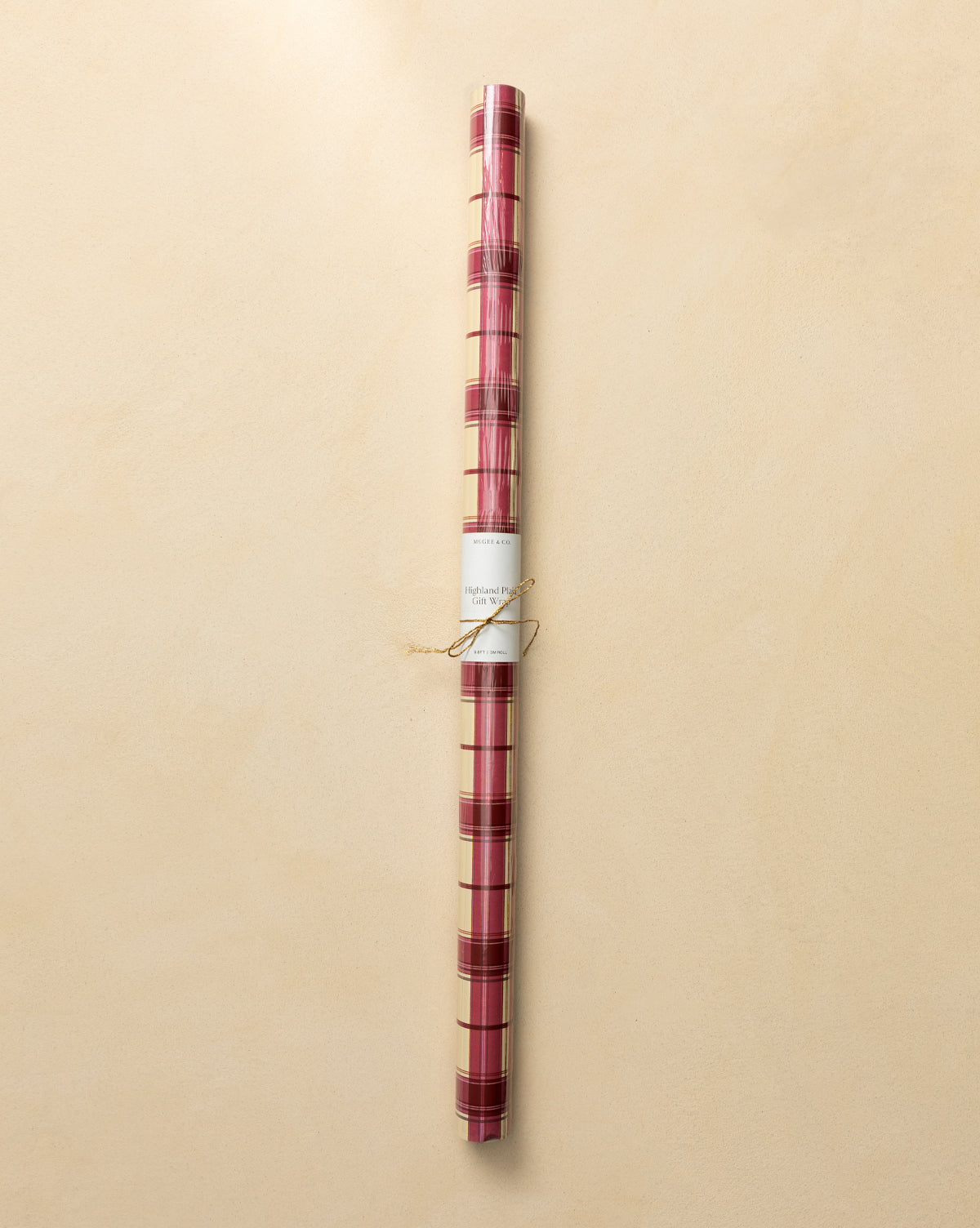 Highland Plaid Gift Wrap in red and gold with a white label and twine, set on a light beige background—ideal festive wrapping paper for the holidays, by McGee & Co.
