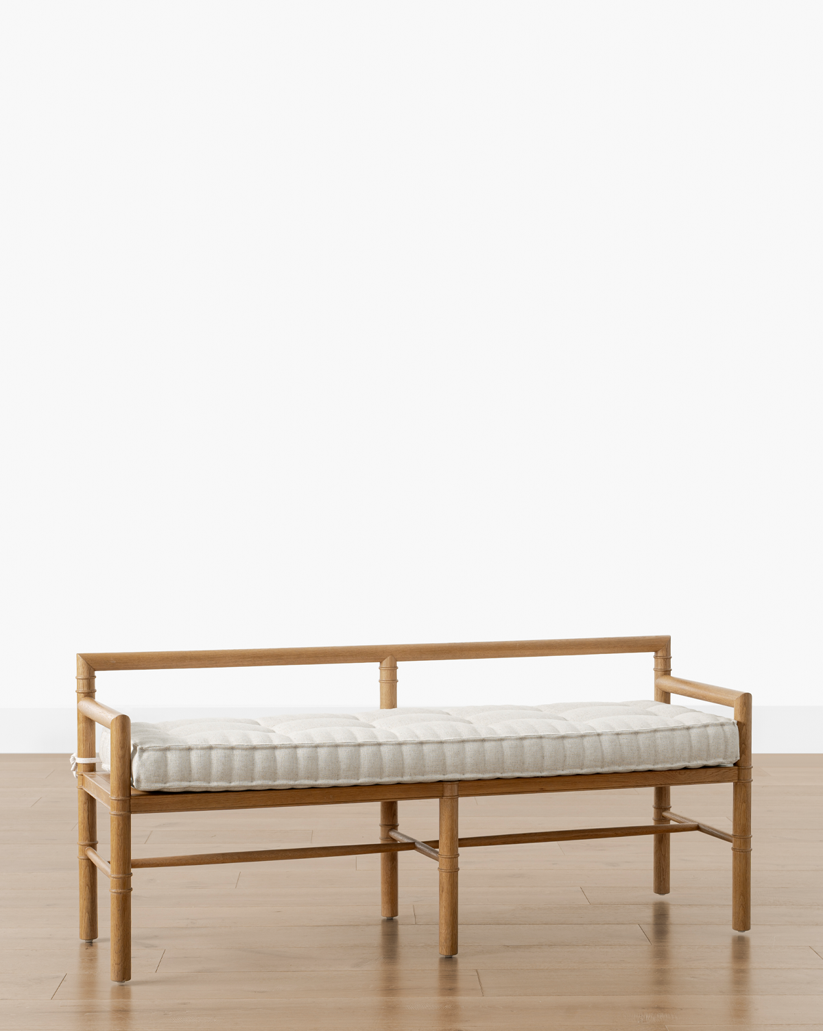The Hindley Bench showcases a solid wood frame and a light upholstered cushion, set on a wooden floor with a plain white background, by McGee & Co.