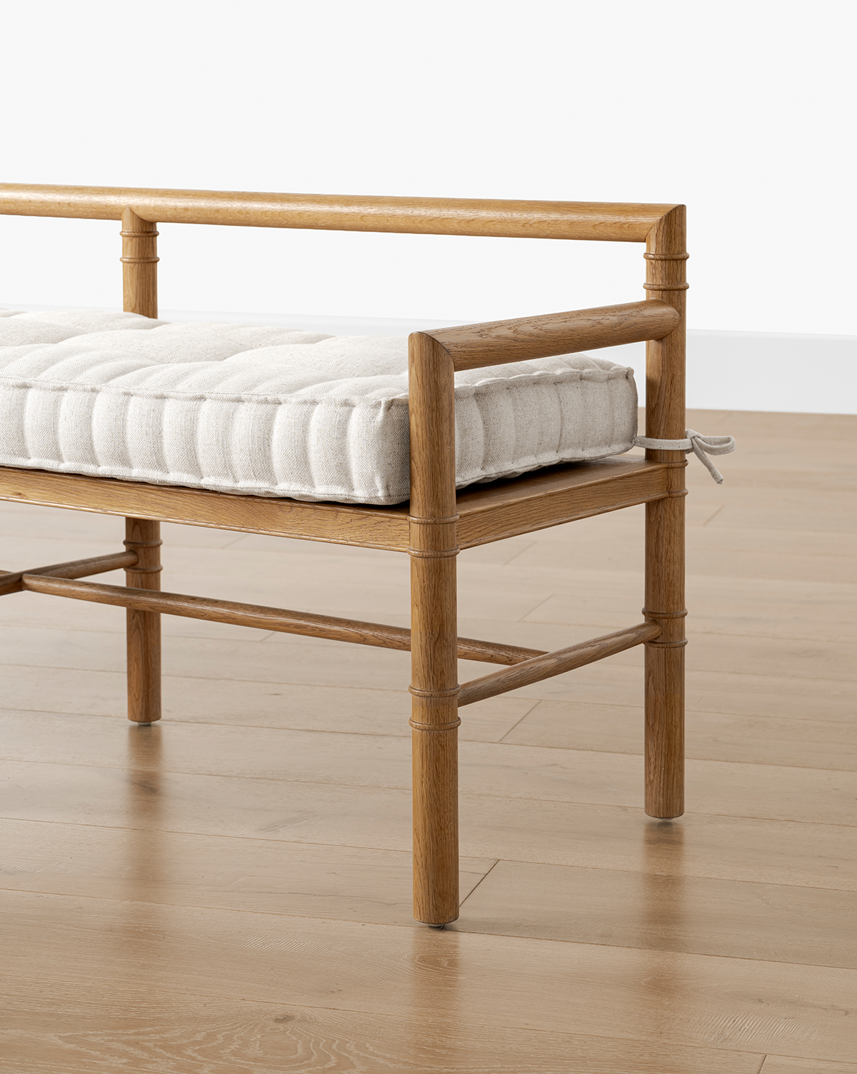 The Hindley Bench features a neatly tufted upholstered cushion, a light brown solid wood frame, and is shown on a light wood floor against a white wall, by McGee & Co.