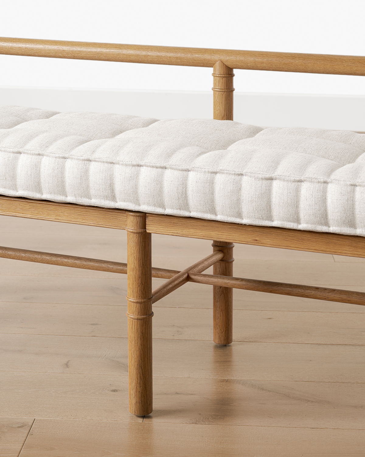 A close-up of the Hindley Bench reveals its solid wood frame, round legs, crossbar support, and a light beige tufted cushion on top, elegantly situated on a light wood floor, by McGee & Co.