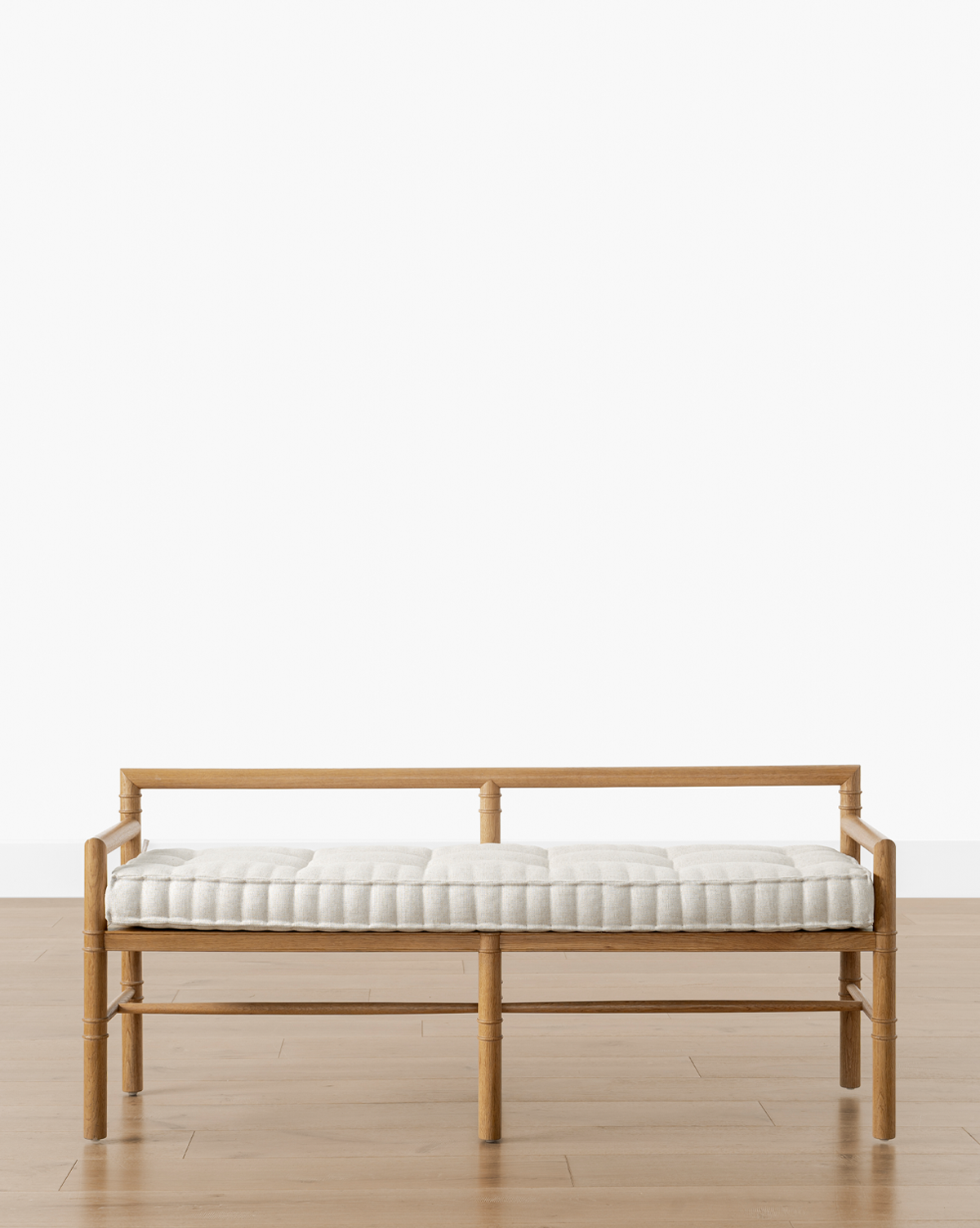 The Hindley Bench features a simple frame and light-colored tufted cushion, shown on a wooden floor against a plain white background, by McGee & Co.